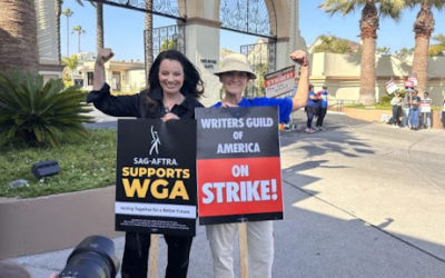 Two People holding signs in support of the Writers Guild of America strike.
