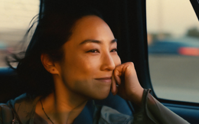 Greta Lee "Nora" riding in a car in a scene from past lives.