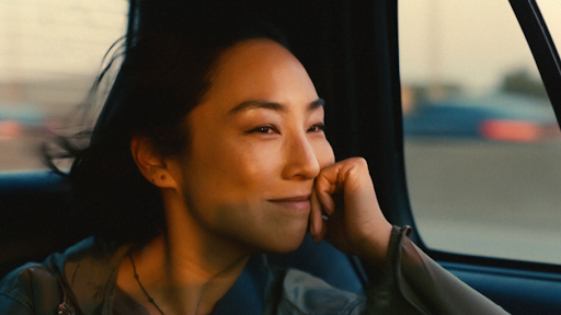 Greta Lee "Nora" riding in a car in a scene from past lives.